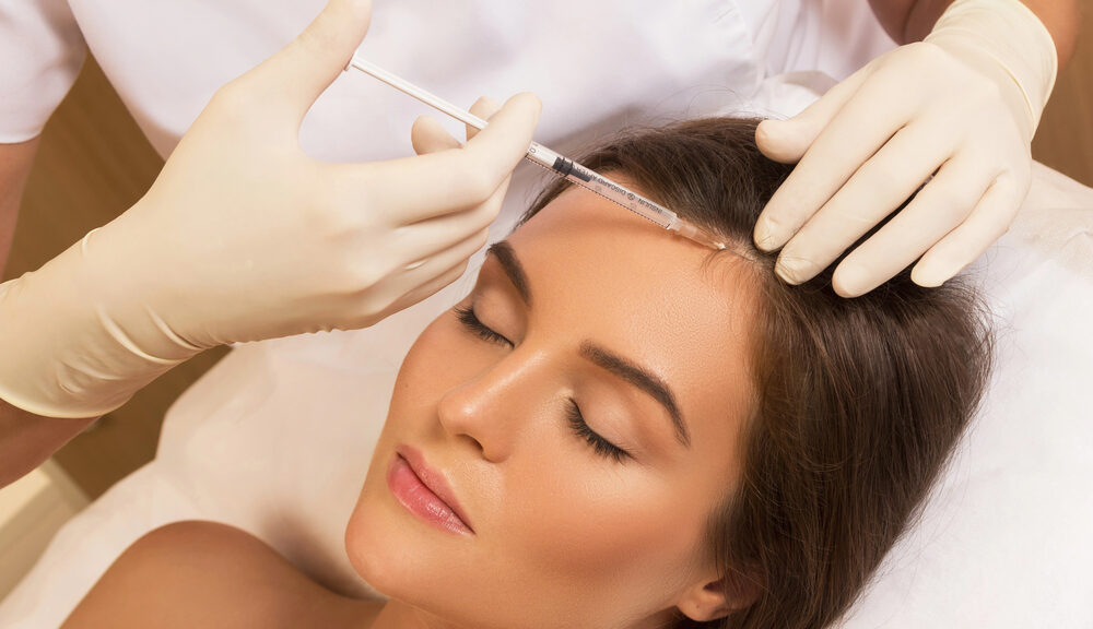Woman receiving forehead injection from gloved practitioner during cosmetic skincare treatment