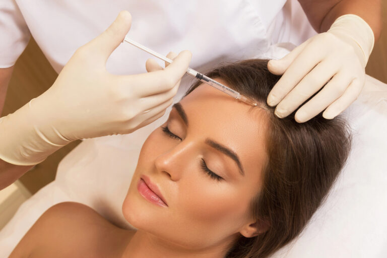 Woman receiving forehead injection from gloved practitioner during cosmetic skincare treatment